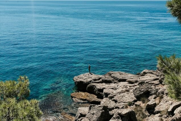 Old man hobby fishing angling standing on big rock stone. senior pensioner catches fish spinning